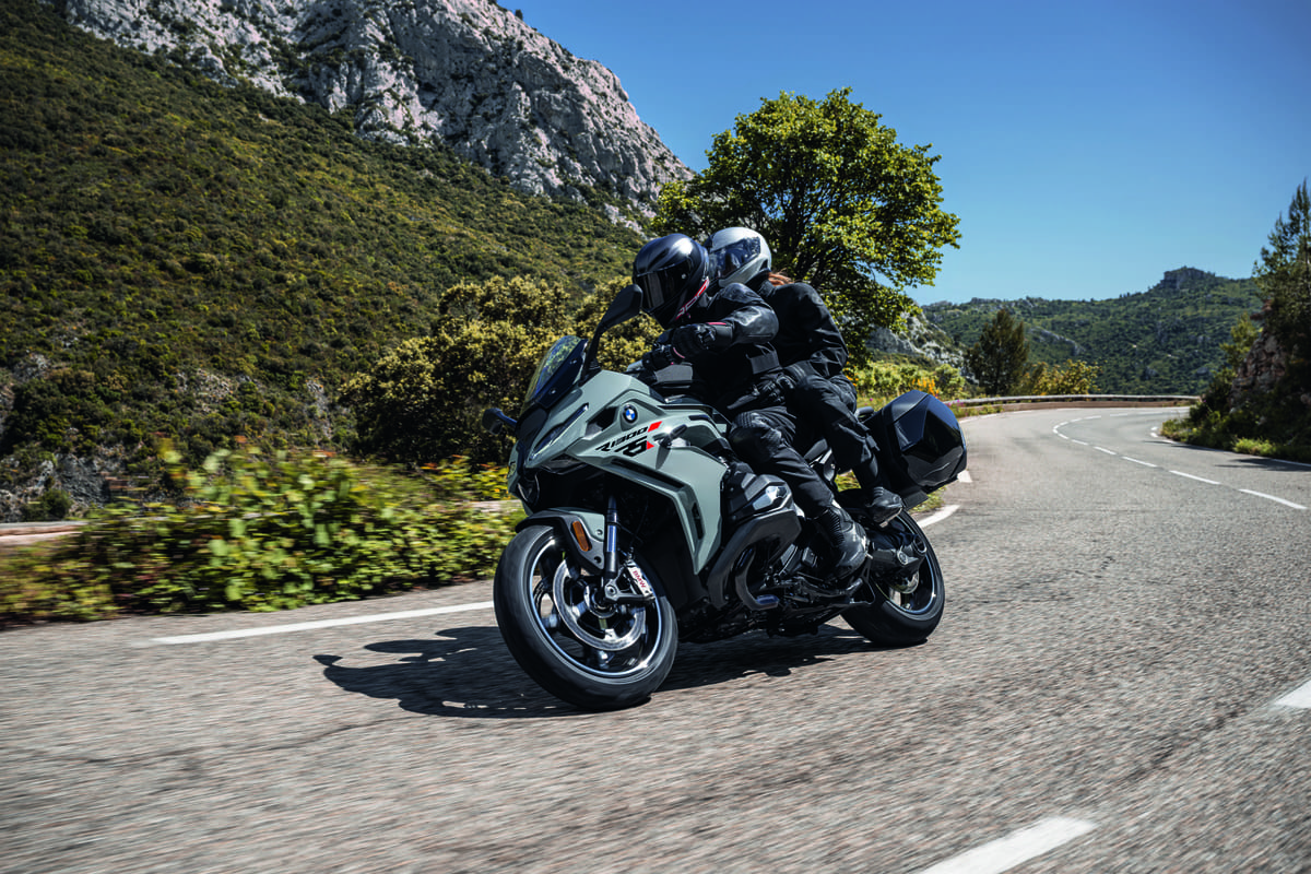 Motorradfahrer und Sozius in einer scharfen Kurve vor einem Bergpanorama