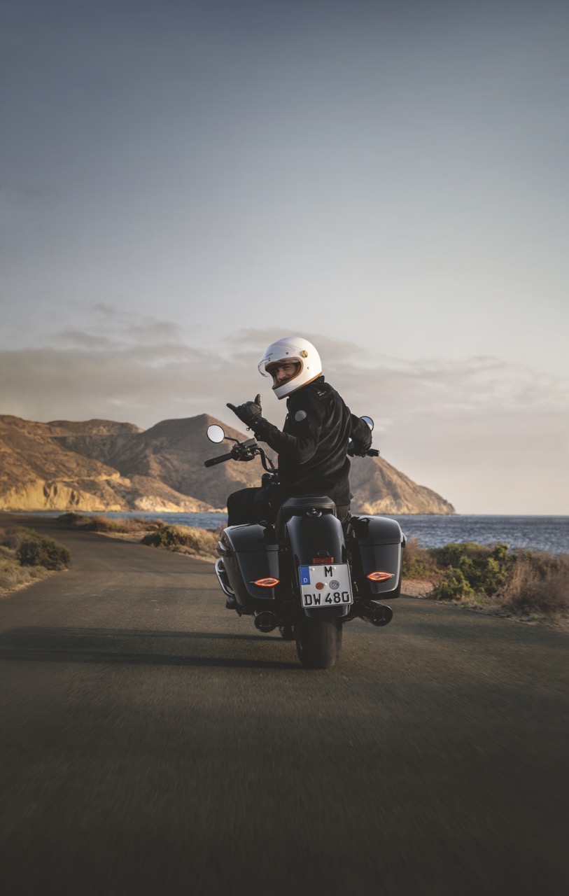 Mann auf einem Motorrad dreht sich w&auml;hrend der Fahrt zur Kamera um und l&auml;chelt.