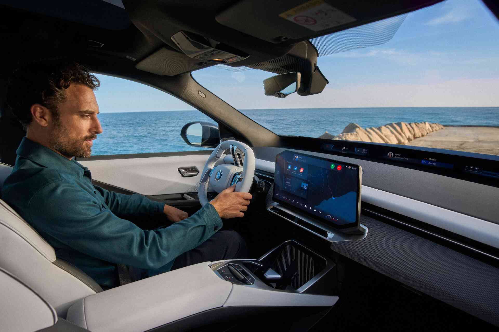 Ein Mann sitzt im BMW iX3 und f&auml;hrt entlang des Meers