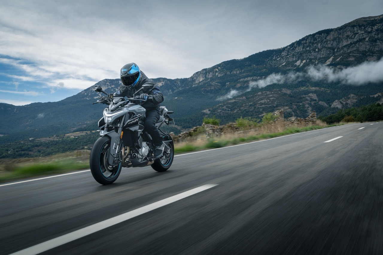 Biker auf einer CFMOTO Maschine f&auml;hrt eine gerade Stra&szlig;e mit Bergpanorama entlang