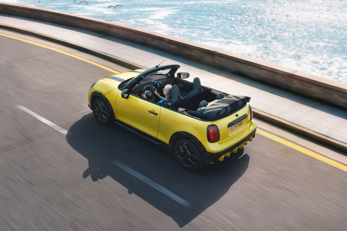 Gelbes MINI Cooper Cabrio mit geöffnetem Verdeck fährt auf einer Straße