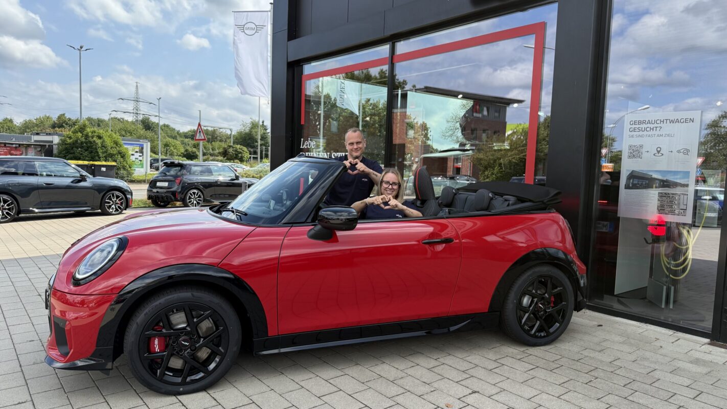 Sarah und Jens in einem roten MINI Cabrio sitzend zeigen Herzen in die Kamera