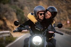 Ein Pärchen fährt zusammen au einem Motorrad. Die Frau die hinten drauf sitzt umarmt den Mann.