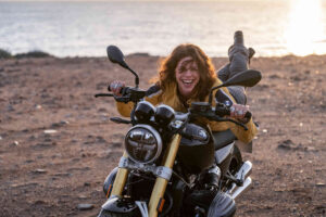 Eine Frau sitzt auf ihrem Motorrad und lacht in die Kamera.
